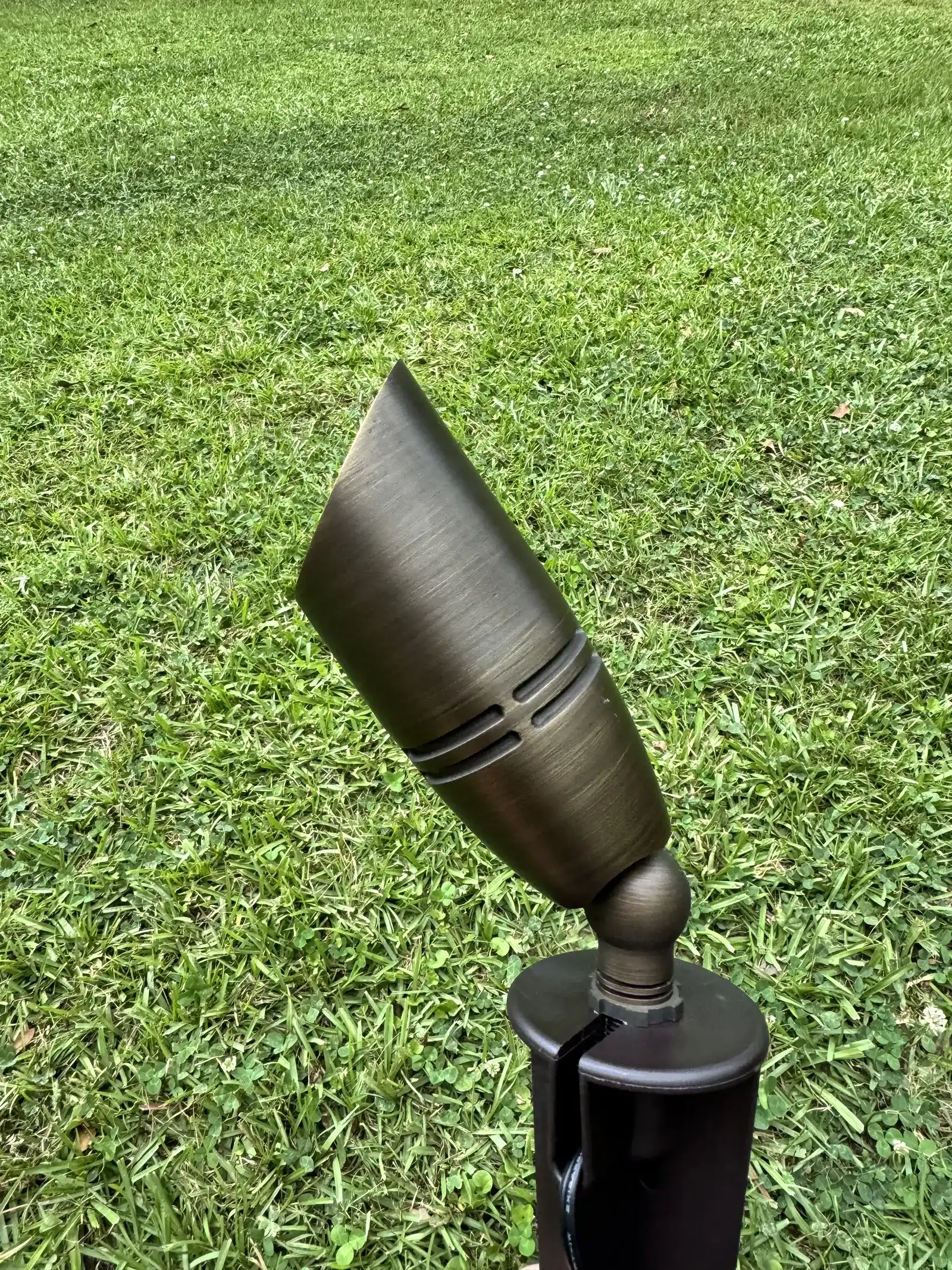 Brass landscape spotlight fixture on a stake in a lawn