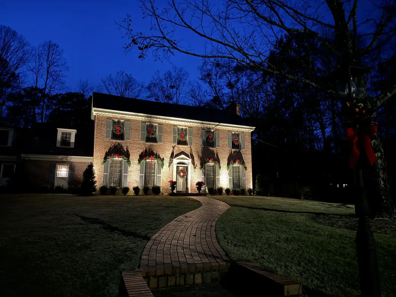 Brick colonial home with uplighting on the facade and a lit curved walkway at dusk