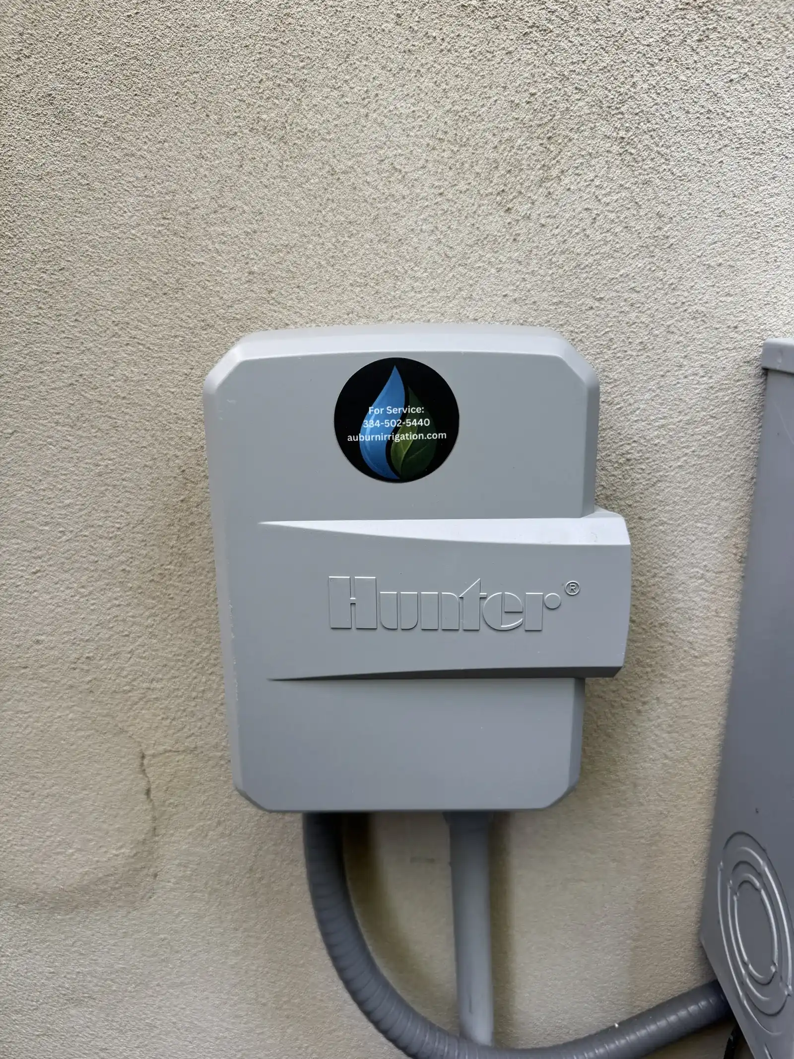 Gray Hunter smart irrigation controller mounted on an exterior stucco wall