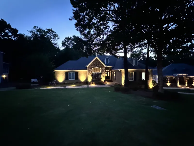 Ranch-style home with warm landscape lighting on the facade and trees at night