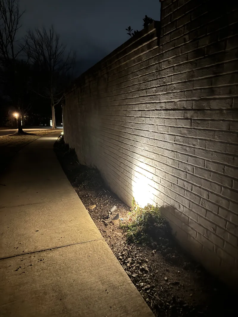 Spotlight washing light up a tall brick wall beside a walkway at night